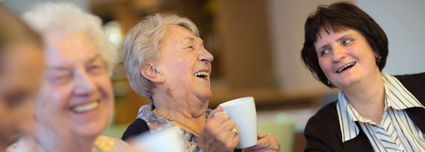 Ein neues Zuhause in einem lebendigen Kiez Bewohnerinnen und Angehörige trinken gemeinsam Kaffee und lachen sie sich gegenseitig an