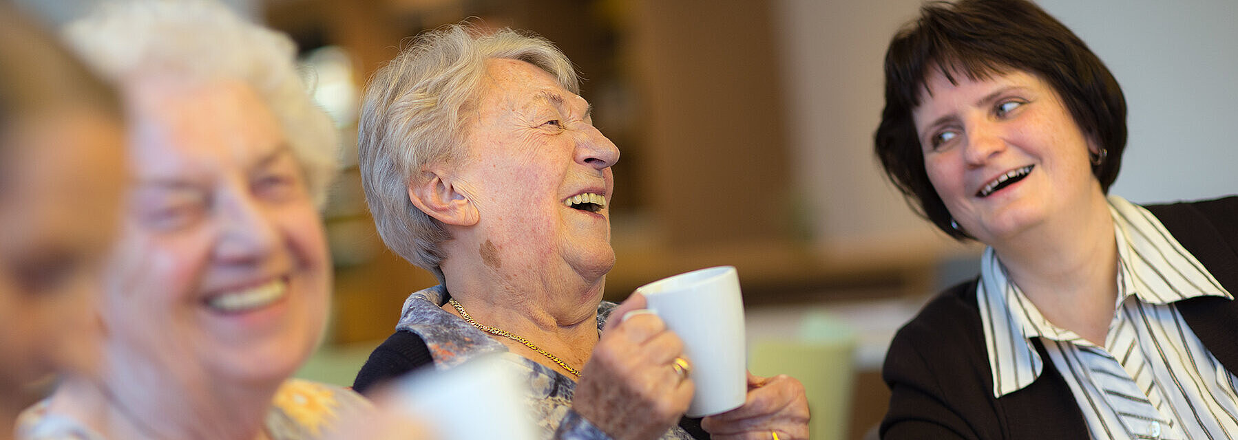 Ein neues Zuhause in einem lebendigen Kiez Bewohnerinnen und Angehörige trinken gemeinsam Kaffee und lachen sie sich gegenseitig an
