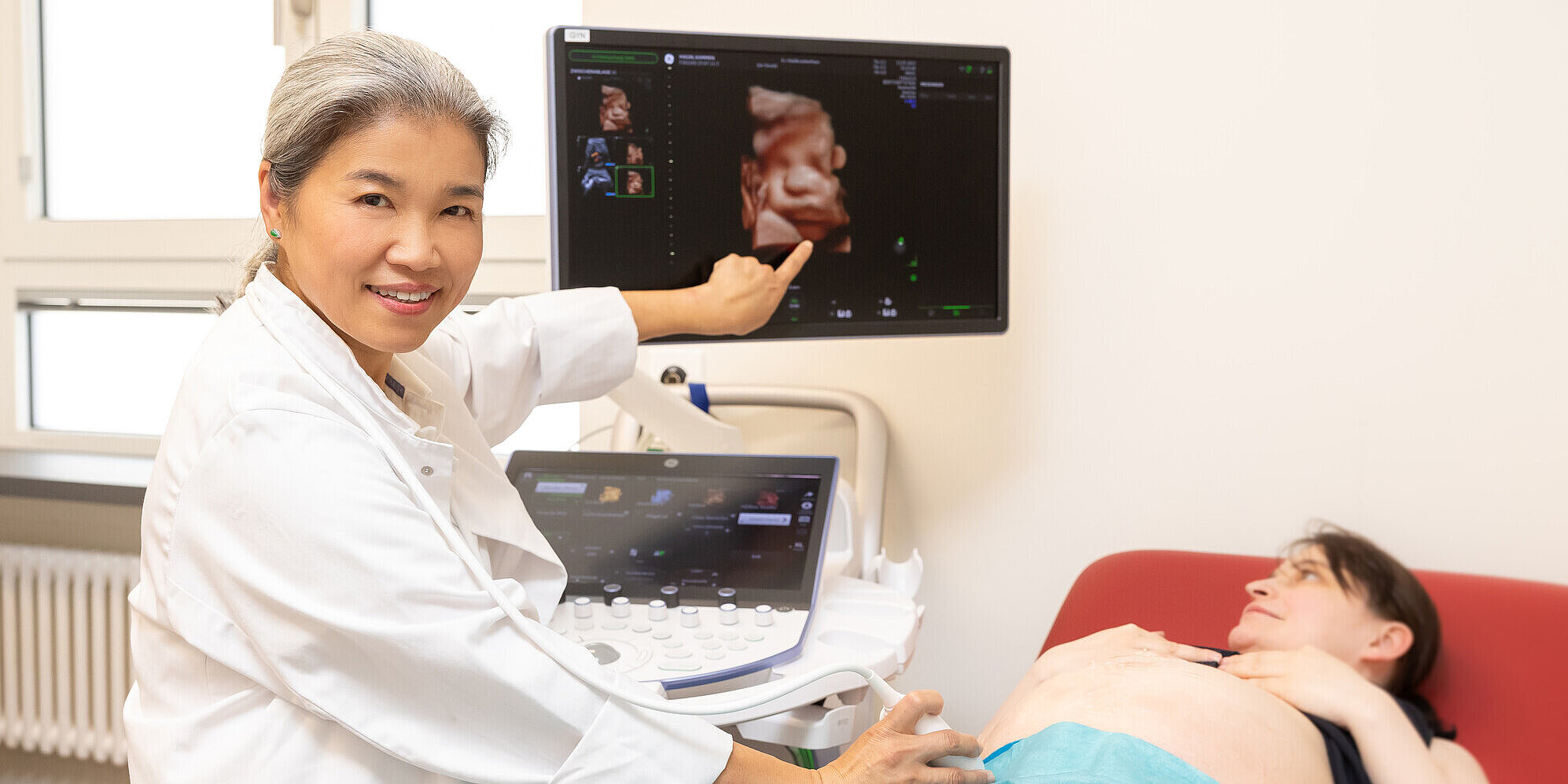 Neu im Team: Prof. Dr. (CN) Weijing Li Ärztin macht Ultraschall bei einer schwangeren Patientin und zeigt auf den Monitor.